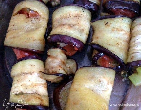 Разогреть духовку до 180 градусов. Сбрызнуть баклажаны оливковым маслом с 2-х сторон. Выложить жареные овощи на полоску баклажана и завернуть. Выложить рулетики на противень для запекания, сверху оставшиеся овощи. Поставить в духовку на 15 минут, чтобы баклажаны подрумянились.