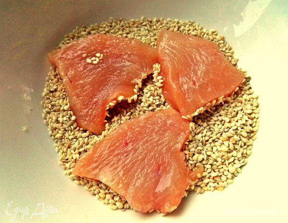 Насыпать кунжут в пиалу и обвалять в нём куриные кусочки.