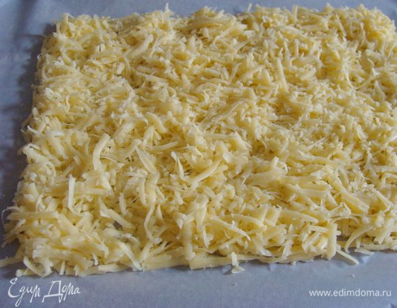 Сыр натереть и выложить в виде прямоугольника на противень на пекарскую бумагу.
