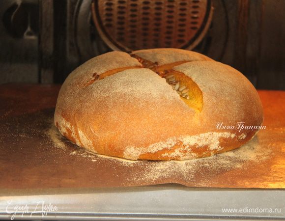 Духовку разогреть до максимума (у меня 250*С) вместе с противнем. Переложить хлеб на горячий противень, быстро сделать крестообразный надрез, насыпать в разрез семечки. Выпекать 10 минут с паром при максимальной температуре, затем без пара при 180*С минут 20-25.