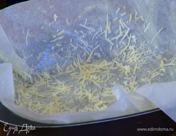 Бумагу для выпечки смазать сливочным маслом, присыпать оставшимся сыром и выложить в небольшую форму для выпечки, так чтобы края бумаги свешивались из формы.