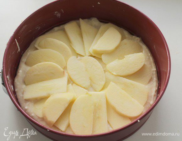 Смажьте форму для выпекания маслом. Половину теста выложите в форму и разровняйте. Яблоко очистить и порезать на тонкие дольки, разложить равномерно на тесто.