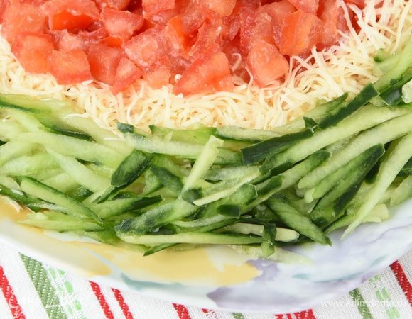 По окружности выложить отложенный натертый сыр. У огурца убрать серединку с семенами. Более жесткую часть огурца вместе с темно-зеленой кожицей натереть на крупной терке и выложить по самому краю салата.
