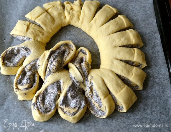 Сформировать ажурный пирог. Для этого 1 "лепесток" из теста отвернуть от себя в центр кольца, слегка разворачивая маковой начинкой вверх. 2 последующие лепестка также осторожно развернуть начинкой вверх, но оставить их с внешней стороны кольца. И так далее по всей окружности; 1 лепесток внутрь, 2 снаружи...