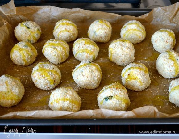 Сформированные таким образом шарики выложить на противень, застеленный пекарской бумагой. Слегка сбрызнуть оливковым маслом и выпекать в разогретой до 190°C духовке 20 минут до золотистого цвета. Готовые шарики выложить на сервировочное блюдо и подавать.  