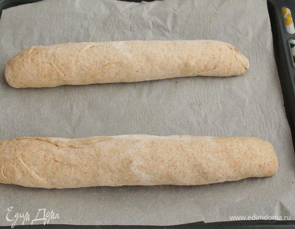 Обминаем и разделим тесто на 2 части. Формируем батоны. Выкладываем на противень, застеленный пергаментом. Накроем полотенцем и ставим в тёплое место на 30 минут.