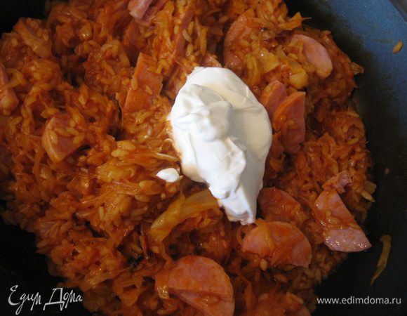 Добавить нарезанные колбаски, сметану и тушить до готовности.