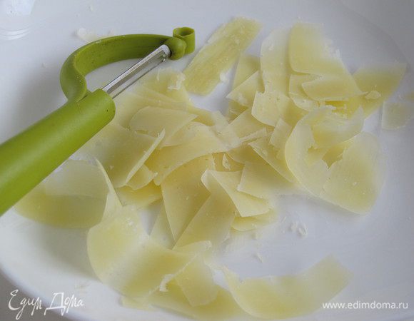 Нарезать сыр тонкой стружкой при помощи ножа для чистки овощей.