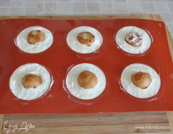 Силиконовую форму поставить на жесткую подставку (у меня разделочную доску), чтобы при переносе в морозилку форма с кремом не деформировалась. Крем Дипломат разложить в формочки в виде полусфер. У меня диаметром 6 см. В итоге крема Дипломат хватило на 12 пирожных-сфер, т.е. получилось 24 полусферы. Плюс «снимала пробу».  Необходимо оставить пару столовых ложек крема – на него мы будем крепить пирожные на основании из бисквита.
В середину положить шу, утапливая в крем до середины. В парные полусферы вставить пустые шу. Потом, когда крем немного подмерзнет, мы их уберём. Выравниваем крем по верхней кромке формы. Убрать форму вместе с подложенной доской минут на 20 в морозилку.
