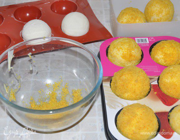 На водяной бане растопить белый шоколад. Наколоть замороженное пирожное-сферу на шпажку (не глубоко!) и окунуть в шоколад, вращая, чтобы стекал лишний шоколад. Подождать несколько секунд, чтобы шоколад еще оставался липковатый, но уже не стекал, и окунуть в бисквитную крошку, обсыпая со всех сторон. 
