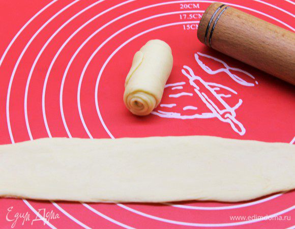 Приступим к розочкам. Скатайте полоску в рулон и разрежьте на две равные части.  В итоге получаем две розочки с одного рулона. Эту процедуру повторите со всем оставшимся тестом. Поместите розочки в центры колец. 