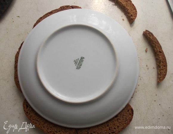 Берем кусочки ржаного хлеба, у меня уже порезанные. Если у вас целая булка, значит порежьте сами. Кладем сверху тарелку и вырезаем по кругу, чтобы тортик у нас получился нужной формы.