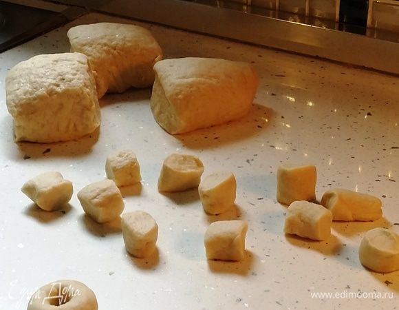 Отделите от шара примерно ⅛ теста, раскатайте в тонкий жгут толщиной с палец, нарежьте на маленькие кусочки. Из каждого кусочка руками на столе скатайте колбаску, а из нее слепите небольшую баранку, соединив и залепив края.