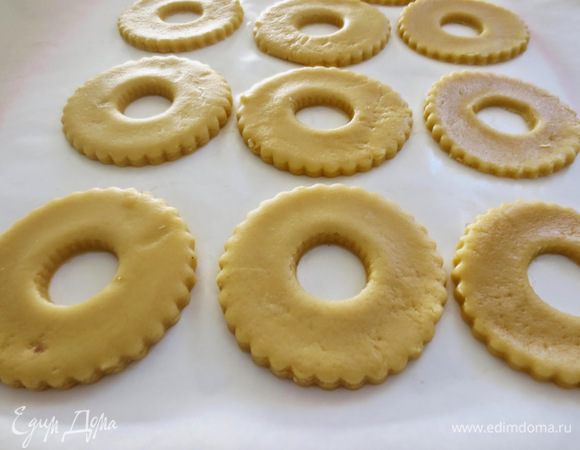Рабочую поверхность присыпать мукой, из теста раскатать пласт толщиной примерно 8 мм. При помощи круглых формочек вырезать кольца. В центре каждого кольца, вырезать  отверстие диаметром 2 см. Противень застелить пекарной бумагой и положить кольца, оставляя расстояние между ними. Противень положить в холодильник на 20 минут.