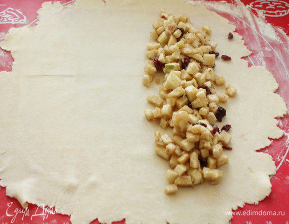 Заранее достаньте тесто, раскатайте каждую лепёшку по очереди на столе, посыпанным мукой, как можно тоньше. Выложите начинку для яблочного штруделя.