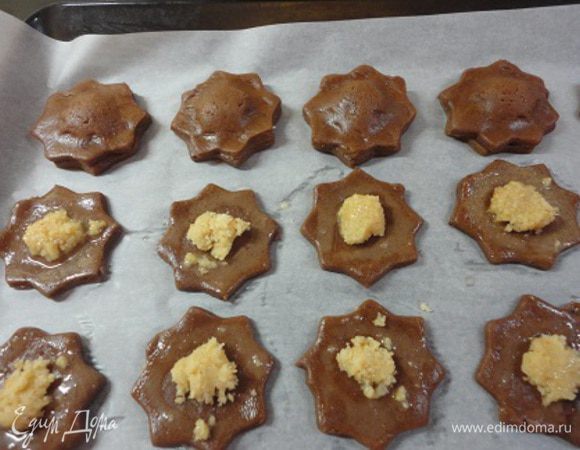 Формочкой с волнистыми краями диаметром 4-5 см вырезать четное количество кружочков. У меня получилось 30 штук. Половину кружочков выложить на лист, выстланный пекарской бумагой. На серединку каждого кружочка положить по кусочку марципановой массы. Свободные края смазать белком (тем, что остался при замесе теста). Накрыть оставшимися кружками и прижать края.