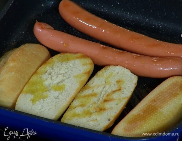 Разогреть в сковороде-гриль оливковое масло, выложить булочки и сосиски и все обжаривать до появления румяных полосок.