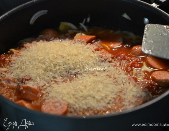 Добавить в блюдо колбасу, томаты баночные порезанные кубиками 400 г, бульон или воду, рис. Довести до кипения, убавить огонь и закрыть крышкой. Готовить до готовности риса примерно 25 минут. Помешиваем.
