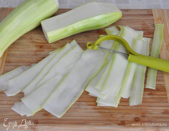 Включить разогреваться духовку до 200 градусов. Противень застелить пергаментом и смазать растительным маслом. 
Молодые кабачки помыть,  если желаете – почистить. Специальной теркой или овощечисткой нарезать тонкие длинные полосы. (Если полосы будут нарезаны толсто, они будут ломаться в процессе сворачивания).
