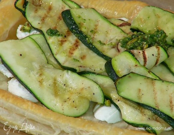 Подпеченный корж вынуть из духовки и разложить на него козий сыр, оставив бортики свободными, сверху выложить часть заправки, затем обжаренные ломтики цукини.