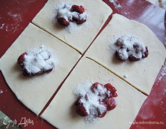 Тесто раскатываем на щедро посыпанной мукой поверхности, само тесто тоже припудриваем мукой, чтобы оно не липло к скалке. 
Для того, чтоб получился эффект слоености не нужно раскатывать тесто очень тонко, 3-4 мм будет в самый раз. Я разделила тесто на 4 части и раскатывала их по одной, каждую деля на 4 квадрата.
Раскатанное тесто нарезаем на квадраты. В центр каждого выкладываем вишни (примерно полная столовая ложка, но это зависит от размера квадрата) и посыпаем сахаром, смешанным с крахмалом (ложку набираем с большой горкой)