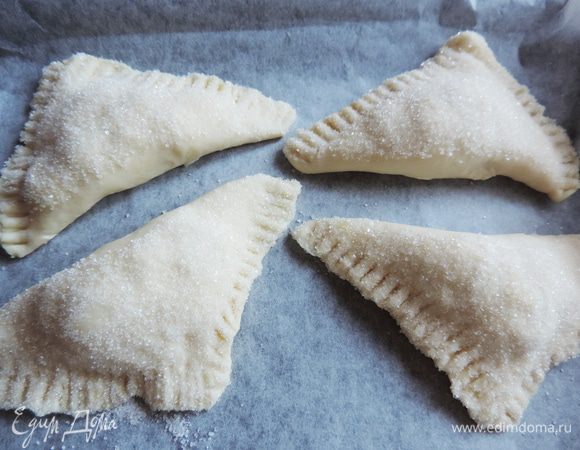 Загибаем тесто по диагонали квадрата, формируя треугольник. Защипываем края. Я дополнительно для крепости и красоты придавливаю их вилкой :)
Каждый треугольничек я опускаю в сахар и придавливаю его, чтоб сахар прилип к тесту. Этот сахар в ингредиентах значится в разделе "Дополнительно". Его понадобится примерно 4-5 столовых ложек.
Выкладываем готовые треугольнички на противень с пергаментом.
На фото первая партия, на второй я для красоты сделала сверху надрезы.