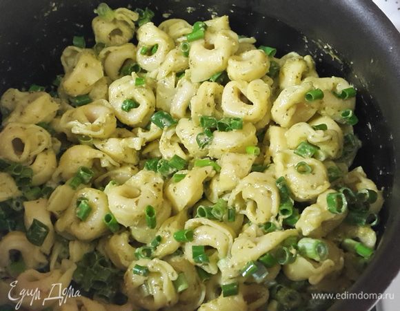 Откидываем готовые тортеллини на дуршлаг. В кастрюльку, в которой они варились, выкладываем соус песто и сразу добавляем тортеллини. Аккуратно перемешиваем, добавляем зеленый лук, накрываем крышкой и прогреваем на медленном огне 2 минуты. Сразу же подаем.