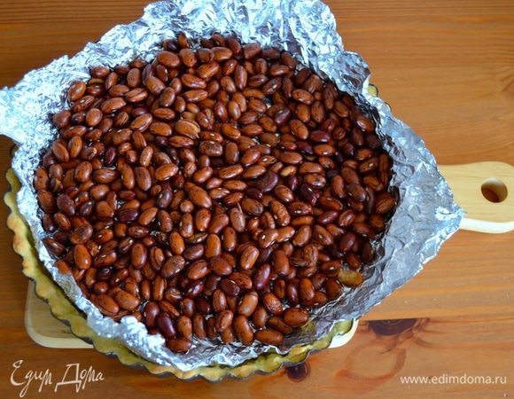 Накройте пекарской бумагой (или фольгой), заполните сухой фасолью или другим "утяжелителем" и поставьте запекаться в разогретую до 190 градусов духовку на 15 минут. Затем достаньте форму с тестом, удалите фасоль и остудите.