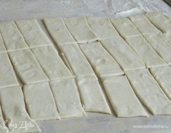 Тесто разморозить и раскатать в одном направлении. Нарезать на полоски, шириной примерно 1,5-2 см, потом на прямоугольники. 
