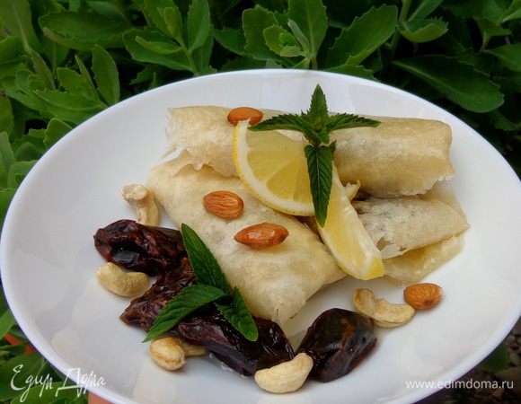 Начинить блинчики и свернуть их трубочкой или конвертиком. Украсить мятой и цельными орешками и финиками. Полить медом.