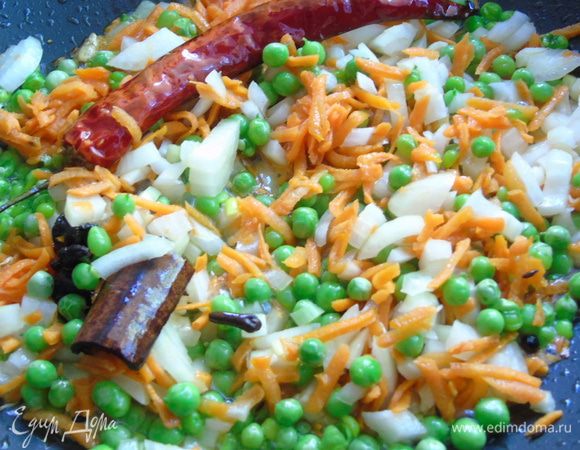 К специям добавьте нарезанный лук, натертую морковь и горошек. Поддержите на огне 2-3 минуты.