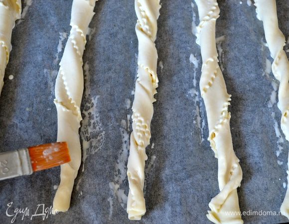 Одновременно пока готовится суп можно приготовить палочки из слоеного теста. Развернуть готовое слоеное тесто, нарезать на полоски шириной 2 см. Взять по две полосочки теста и свернуть-завернуть их между собой. Выложить на противень, застеленный пекарской бумагой. Смазать смесью яичного желтка и сливок (у меня на этот раз просто сливки) и присыпать тертым сыром (или кунжутными семечками, как у меня).