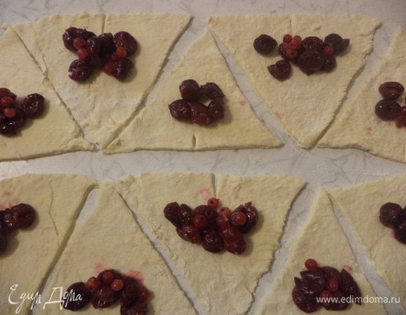 С широкой стороны каждого треугольника сделать надрез длиной около 1 см, затем подвернуть нижнюю часть в середину.
Выложить на тесто начинку и свернуть рогаликом, немного закруглив уголки.