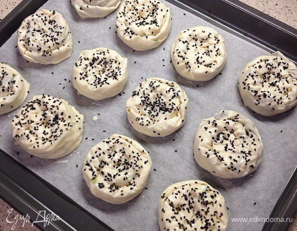 На треугольники теста сначала наливать немного соуса (можно смазывать кисточкой всю поверхность, соуса не жалейте особо) затем выкладывать начинку из шпината, распределяя ее по всей поверхности. Вот начинки надо брать немного. Затем сворачивать треугольники от большого края к маленькому (как рогалики или круассаны). Получится такая тонкая, длинная колбаска и уже ее сворачиваем по спирали, чтобы получились такие булочки-розочки. Поверхность булочек смазываем тем же соусом, что и внутри. Посыпаем черным кунжутом (можно и белым обычным).