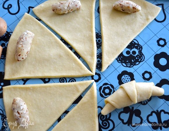 Из каждого кусочка марципановой начинки скатайте маленькую колбаску и выложите на тесто с более широкого конца. Сверните рогалик, наподобие круассана. Таким же образом приготовьте все остальные рогалики.