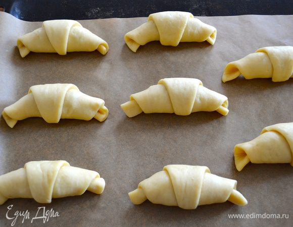 Выложите рогалики на застеленный пекарской бумагой противень и дайте постоять, накрыв полотенцем 10 минут. За это время включите прогреваться духовку на 190-200 градусов. Через 10 минут с помощью кисточки смажьте рогалики сливками (или яичным белком, кому как больше нравится!)