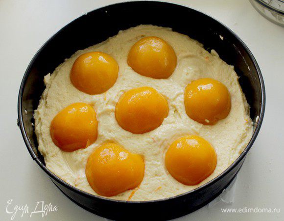 Распределите тесто по форме, разровняйте, сверху разложите половинки персиков, слегка вдавливая их в тесто.