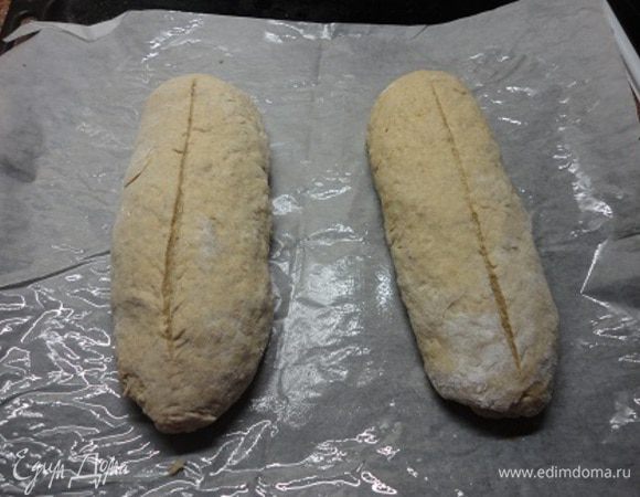 Из подошедшего теста сформируйте два батона, выложите на противень, выстланный бумагой для выпечки. На батонах сделайте надрезы. Дайте еще подойти.
