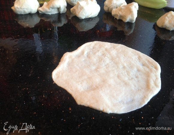 Тесто разделите на 8 частей. Смажьте маслом поверхность стола и слегка раскатайте тесто.