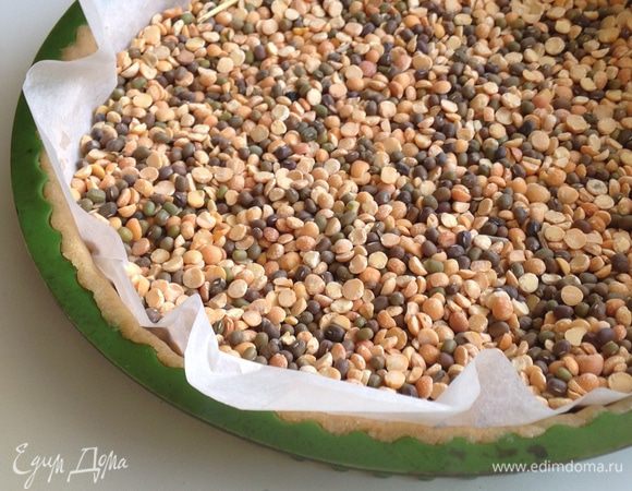 Закрыть тесто листом бумаги и насыпать сухую фасоль или горох. Поставить основу в духовку и выпекать 15 минут при 160 град.