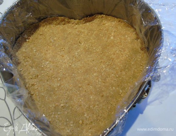 Форму застелить пленкой, так будет легче извлечь чизкейк, и выложить печенье, перемешанное с растопленным маслом. Хорошо утрамбовать. Уберите в холодильник.