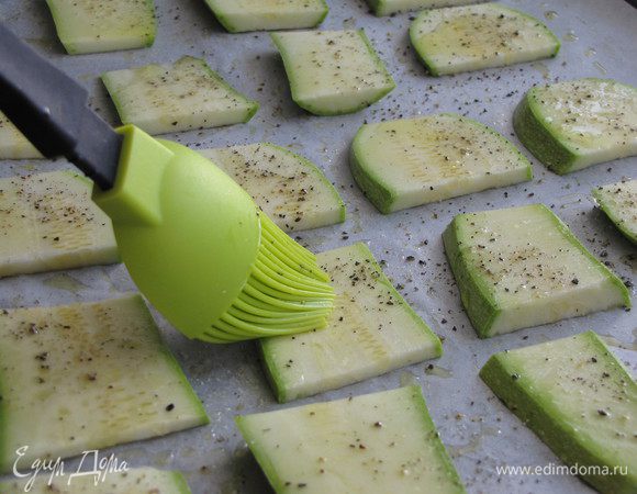Кабачки, не очищая от кожуры, нарезать пластинками, толщиной 0,5 см. Противень застелить пекарской бумагой и немного смазать оливковым маслом. Выложить подготовленные кабачки, посолить и поперчить по вкусу. Смазать сверху оливковым маслом. Поставить в духовку и запекать при 180 градусах минут 20, до зарумянивания.