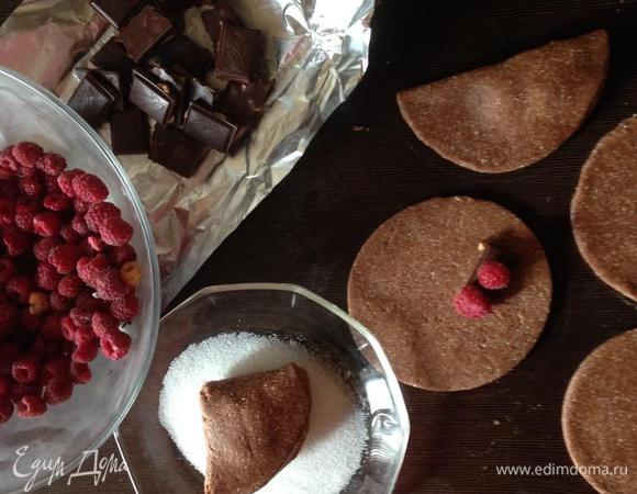 Затем визуально делим круг на 4 сектора и в правый нижний кладем начинку из дольки шоколада (у меня темный с дробленым лесным орехом) и пары ягод малины. Складываем пополам, а затем еще раз пополам (думаю, техника знакомая каждому дому). В миску насыпаем сахар и обмакиваем печенье стороной, где больше слоев теста. Хорошенько припечатываем, чтобы сахара хватило, так как в тесте его немного, и выкладываем на противень, застеленный пергаментом или фольгой.