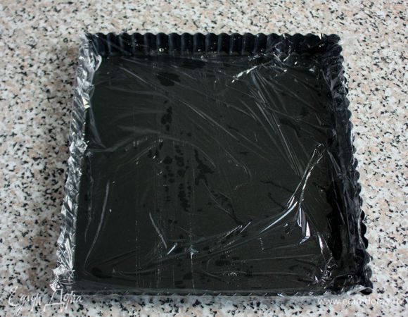 Форму для выпечки ополоснуть холодной водой и выложить изнутри пищевой плёнкой так, чтобы края свисали по бокам.

