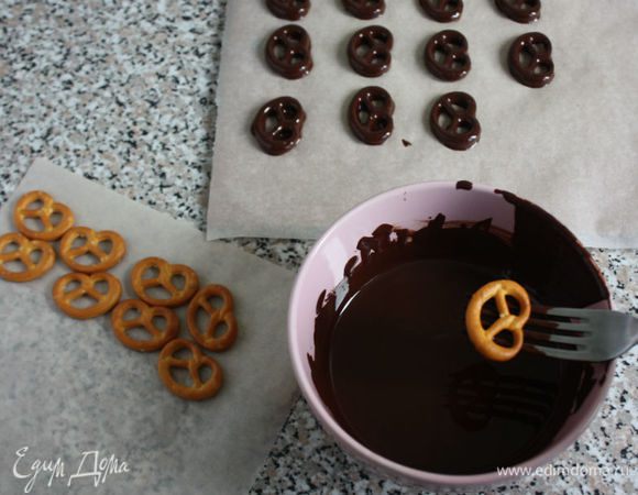 На водяной бане расплавить 150 г шоколада. Вилкой погружайте поочередно в него мини-бретцели, дайте стечь излишкам шоколада и выкладывайте их на пергамент. Вам будет удобнее, если пергамент постелить на разделочную доску. Вместе с доской перенесите глазированные бретцели на 10 мин в холодильник.

