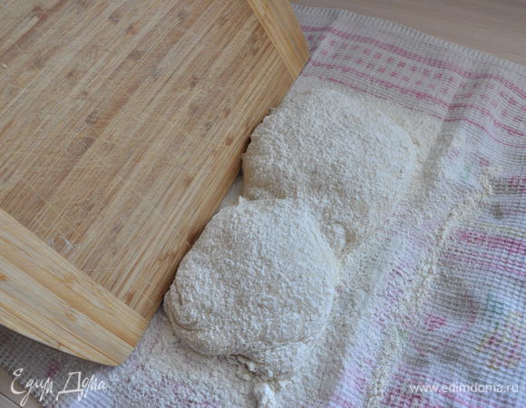 Чтобы аккуратно, не выпуская  драгоценных пузырьков, перенести чабатту на противень, надо поднести к ней разделочную доску или кусок плотного картона.
Быстрым движением полотенца, на котором лежало тесто, переверните его на эту доску. Чабатта при этом не должна сильно плюхнуться. Вот здесь будет видно насколько вы не пожалели муки для присыпки полотенца.
Сверху окажется поверхность, лежащая на полотенце, а швы окажутся снизу.