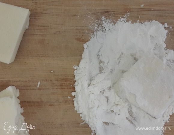 Сыр нарезать крупно. Обмакнуть сначала в муку, затем в соль. В сковороду наливаем 1 столовую ложку растительного масла и кусочек сливочного, выложить сыр и обжарить до золотистого цвета (буквально 15 секунд с каждой стороны). Выкладываем на бумажное полотенце. 
Из апельсина выжимаем сок, добавляем его в сковороду, где жарился сыр. Готовим, пока не загустеет. 
Духовку разогреть до 180 градусов. Выложить на противень сыр, полить соусом. Посыпать сверху сахаром и кунжутом. Выпекать 15–20 минут