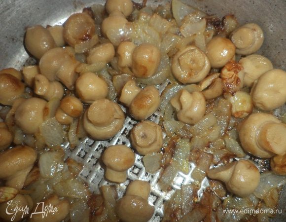 Луковицу нарезать мелкими кубиками, обжарить на растительном масле до прозрачности.
Мелкие маринованные шампиньоны откинуть на сито, слить жидкость, а грибочки добавить в сковороду к луку и обжарить до зарумянивания. 