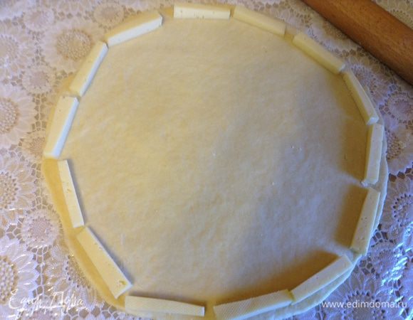 Раскатать тесто в круг, по краю выложить остаток сыра нарезанный брусочками.
