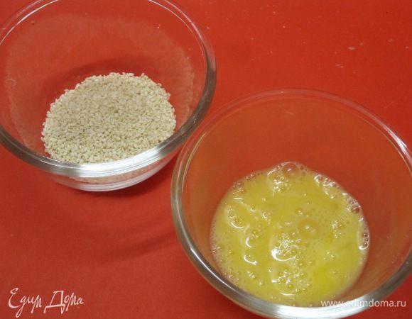 Слегка взбить желток яйца, кунжут высыпать в тарелочку.